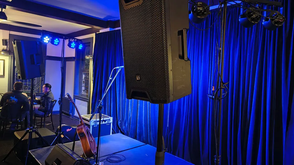 A speaker on a stand beside a small stage with blue curtains and lights