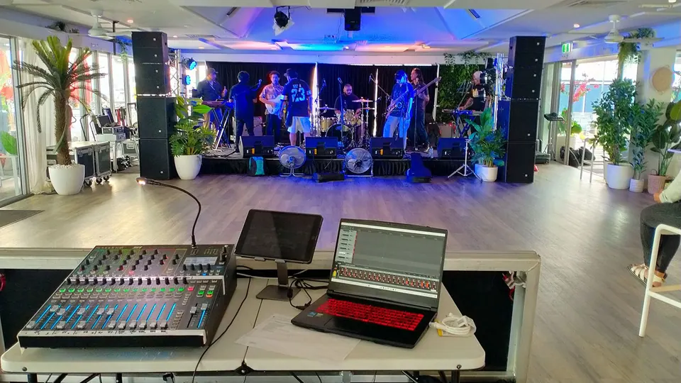 A band on a waterside deck stage, seen from the mixing desk