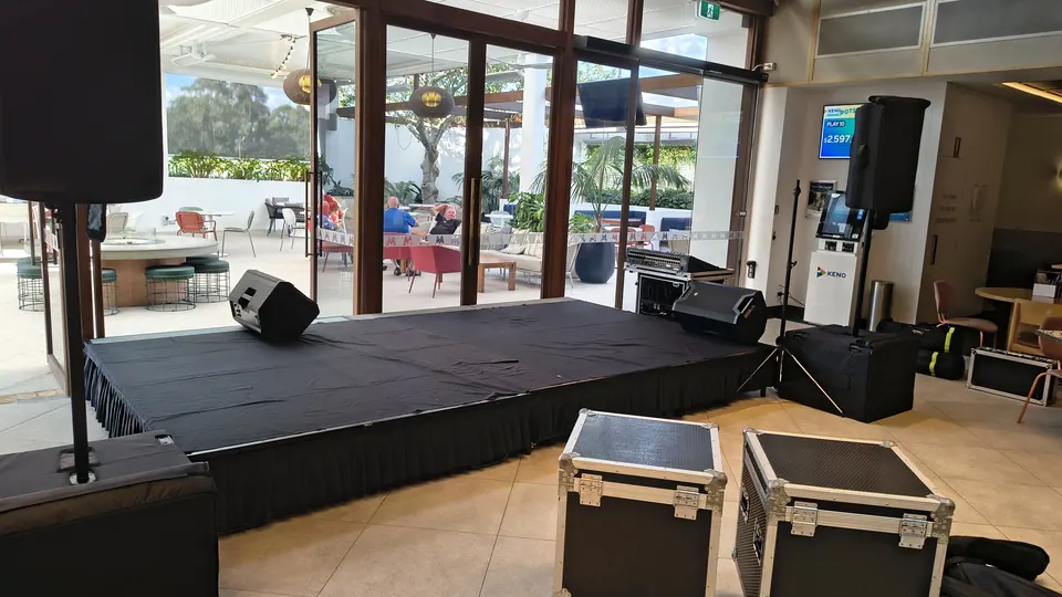 A stage being set up in a bright venue, with speakers and road cases