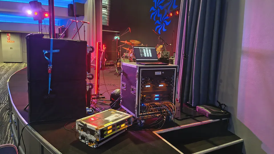 A speaker stack, amp rack and stage boxes at the side of the stage